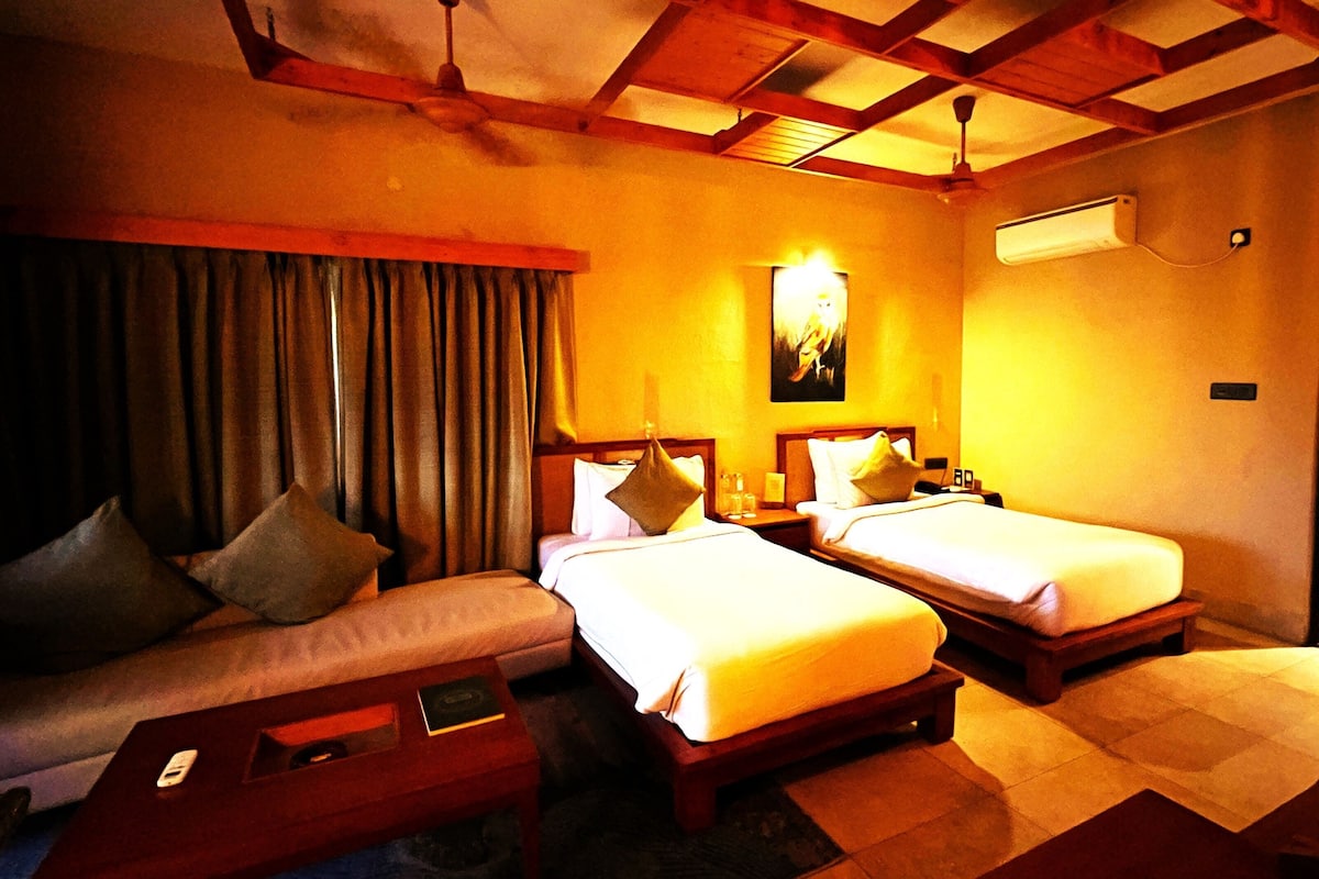 A hotel room with two beds, a sofa, a coffee table, and a ceiling fan.