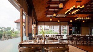 Een restaurant met houten meubels, grote ramen en hangende lampen.