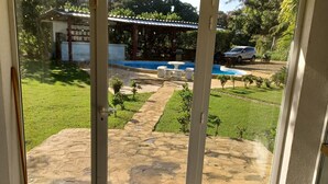 Una stanza con una porta finestra scorrevole che si apre su una zona esterna con piscina, giardino e un'auto parcheggiata nelle vicinanze.