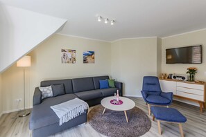 Ein modernes Wohnzimmer mit grauem Sofa, einem runden Couchtisch, einem blauen Sessel und einem an der Wand befestigten Flachbildfernseher.