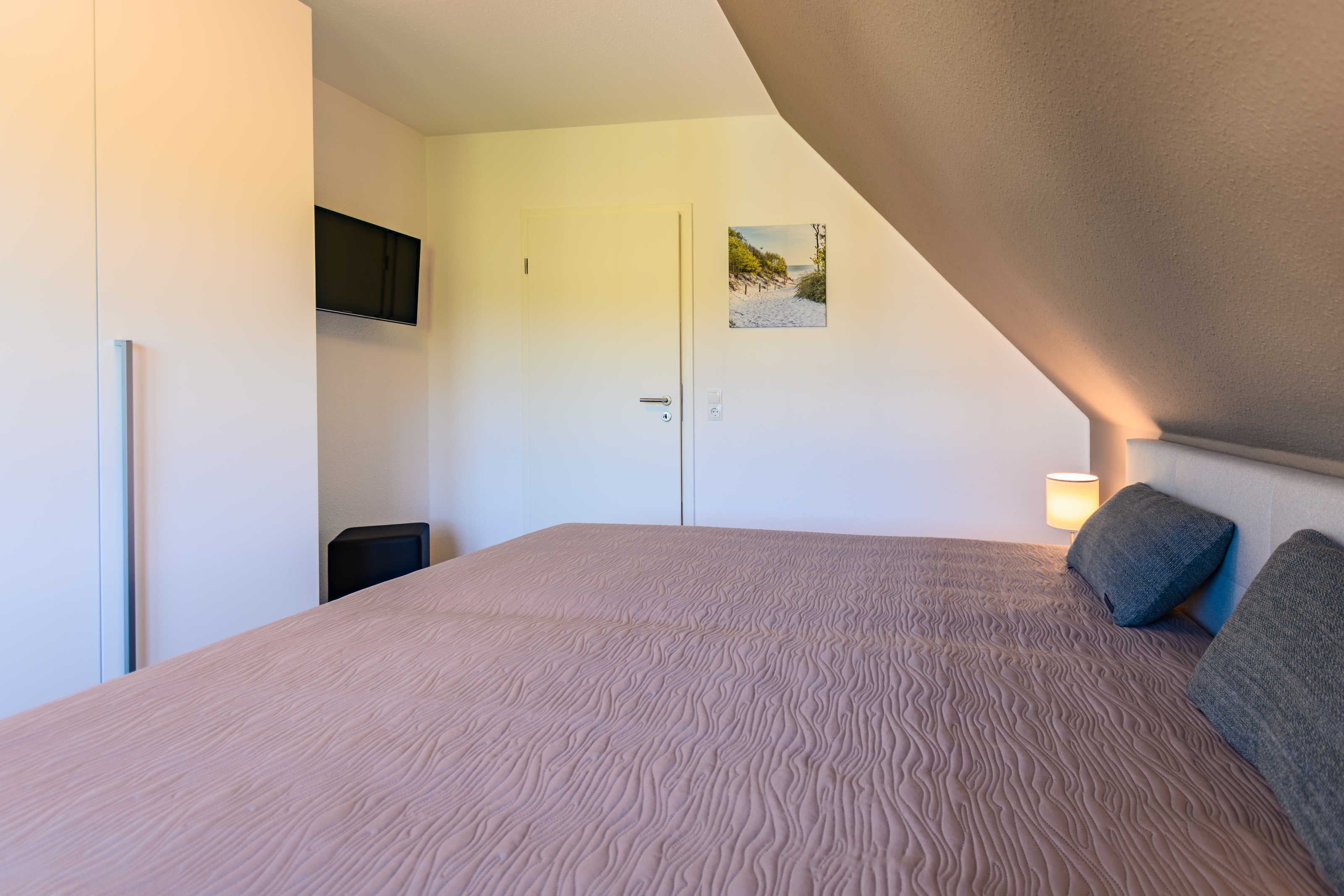 A bedroom with a large bed, a flat-screen TV mounted on the wall, a door, and a small picture.