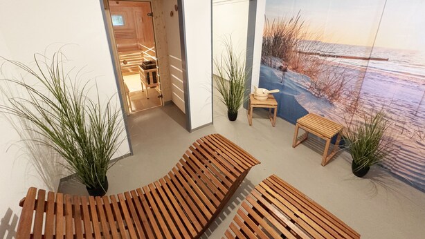 Um interior moderno com bancos de madeira, plantas em vasos e um grande mural na parede retratando uma cena de praia.