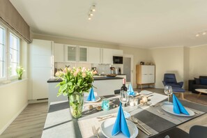 A modern dining area with a table set for four, a vase of flowers, and a kitchen in the background.