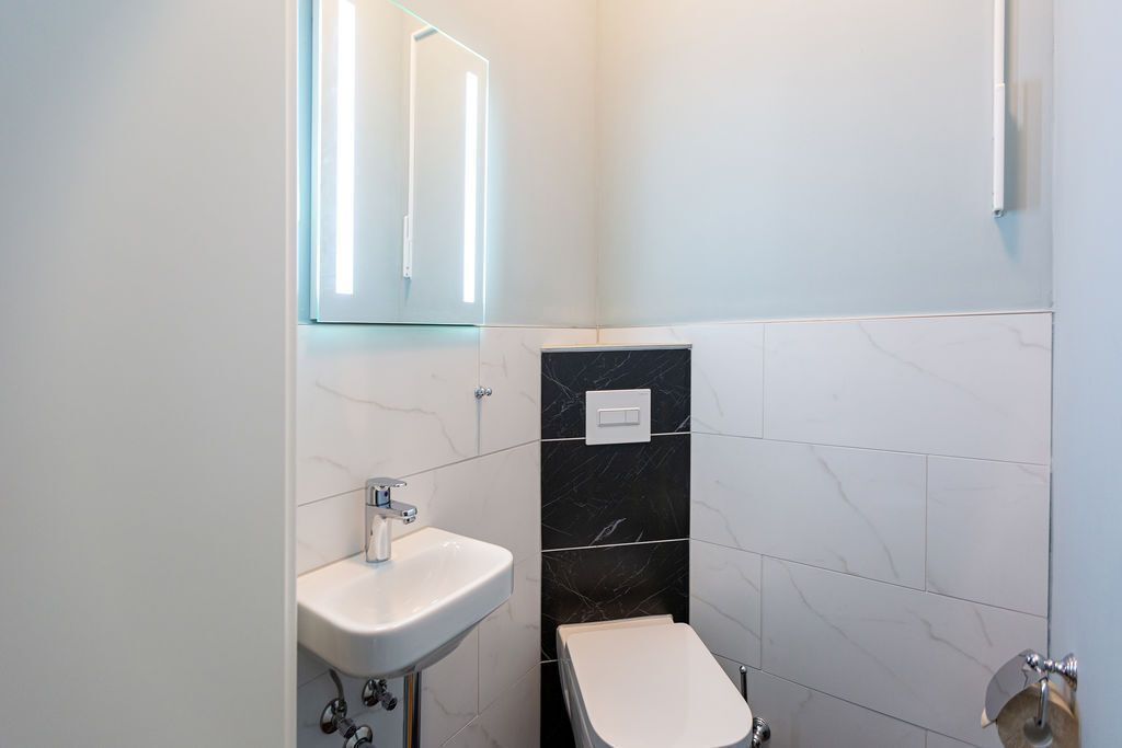 Ein modernes Badezimmer mit einem weißen Waschbecken, schwarzen Marmorfliesen und einer Toilette.
