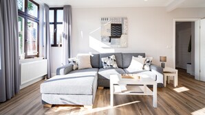 Ein modernes Wohnzimmer mit Ecksofa, Couchtisch und großem Fenster mit Vorhängen.