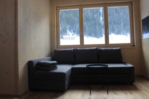 Una habitación con un sofá de color oscuro, una mesita redonda y un amplio ventanal con vistas a un paisaje nevado.