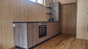 Une cuisine avec des meubles de rangement en bois, un four encastré et une fenêtre au-dessus de l’évier.