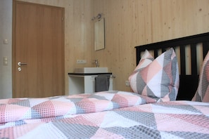 Ein Schlafzimmer mit Holztür, einem Nachttisch mit Spiegel, einem Waschbecken und einem Bett mit gemustertem Patchwork-Quilt.