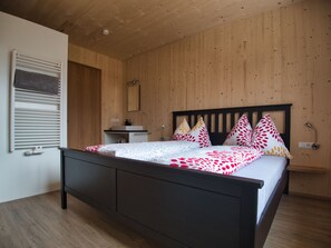 Un dormitorio con techo de madera, una cama con ropa de cama estampada, una mesita de noche y un espejo.