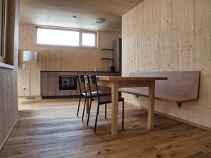 Een moderne keuken met houten kastjes, een ingebouwde oven en een eethoek met een tafel en stoelen.