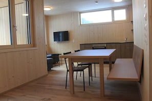 Ein Holzinterieur mit Esstisch, Stühlen, einer Bank, einem an der Wand montierten Fernseher und einem Fenster.