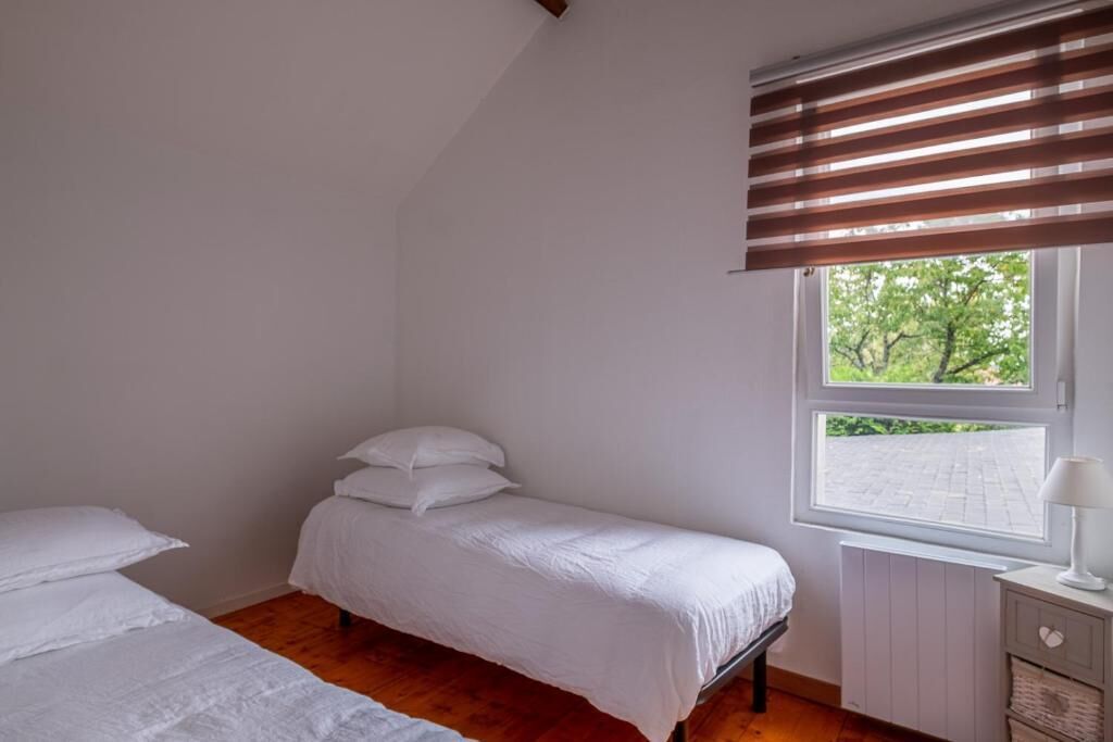 Une chambre avec un lit simple, une fenêtre avec des stores, un radiateur et une table de chevet avec une lampe.
