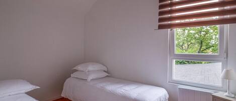 Un dormitorio con una cama individual, una ventana con persianas, un radiador y una mesita de noche con lámpara.