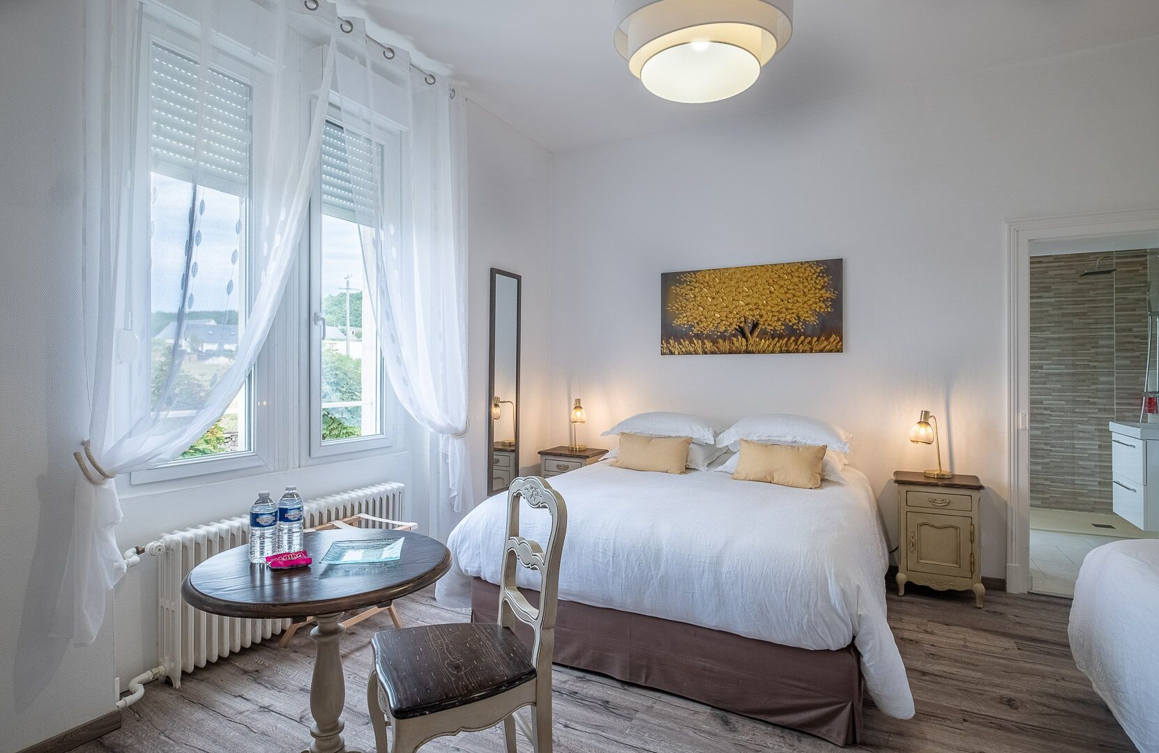 Una camera d'albergo con un letto, comodini, una sedia, un tavolino rotondo e una finestra con tende.