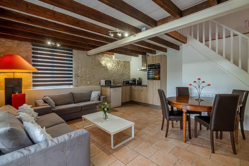 A modern living room with a sofa, coffee table, and dining area. There is a kitchen with appliances and a staircase.