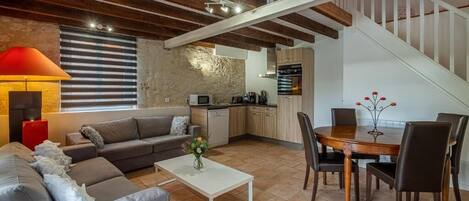 A modern living room with a sofa, coffee table, and dining area. There is a kitchen with appliances and a staircase.