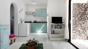 Une cuisine moderne avec des meubles blancs, un plan de travail de couleur turquoise et un téléviseur posé sur une étagère blanche.
