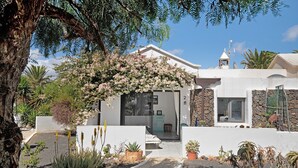 Une maison à l’extérieur blanc, avec un mur en pierre et un jardin où poussent différentes espèces de plantes.