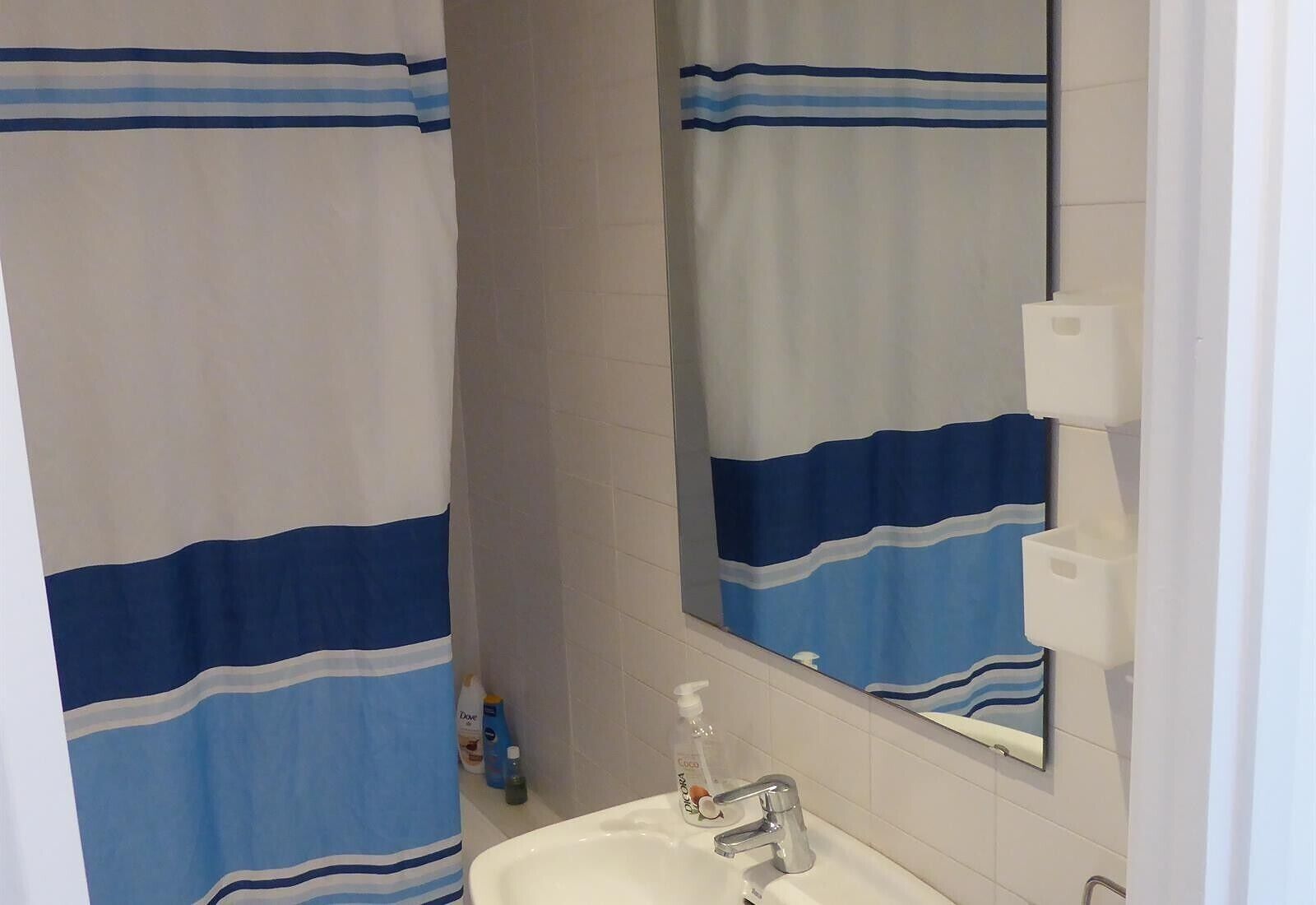 Ein Badezimmer mit einem weißen Waschbecken, einem Spiegel und einem Duschvorhang mit blauen und weißen Streifen.