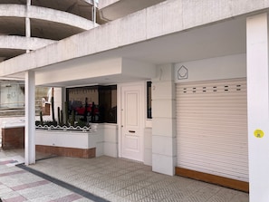 Un edificio con un obturador cerrado, una puerta y una ventana que refleja un coche y cactus.