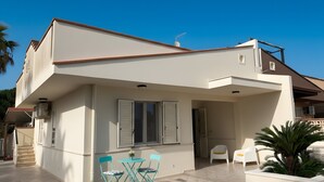 Une maison moderne à deux étages, dotée d’un balcon, d’une petite table avec des chaises et d’une plante en pot.