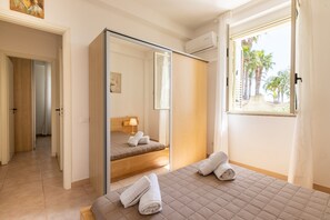 Quarto de hotel com cama, espelho, janela com cortinas, porta e corredor.