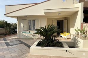 Uma casa moderna com um alpendre, um pequeno jardim e mobiliário de exterior.
