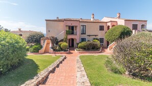 Un bâtiment à deux étages, doté d’un toit recouvert de tuiles, d’une entrée centrale avec un escalier et d’un jardin bien entretenu avec un chemin pavé.