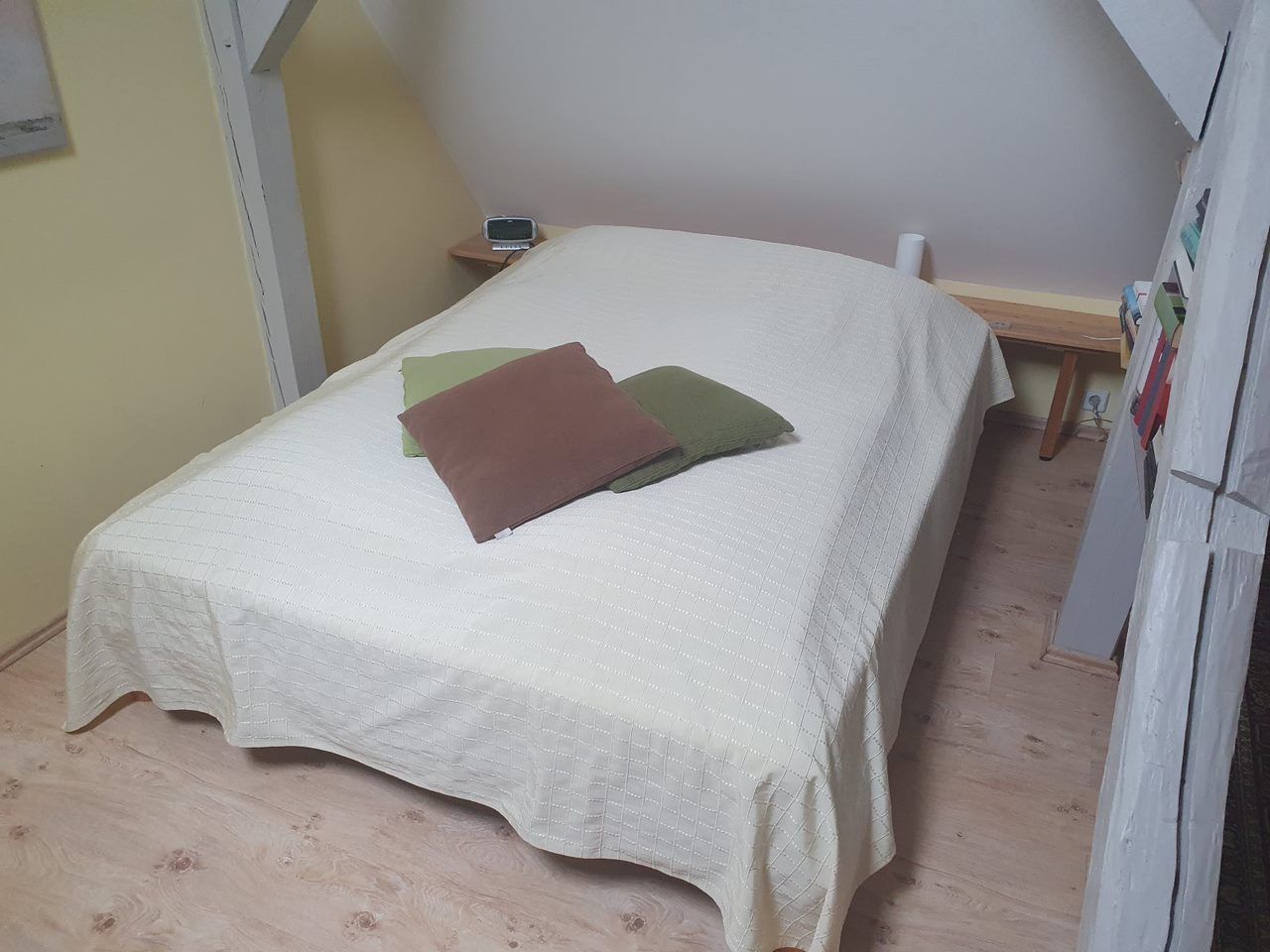 Ein Einzelbett mit weiß gesteppter Bettdecke, ein Nachttisch aus Holz mit einem Mobiltelefon und ein Holzboden.