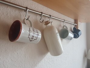 Ein Metallregal mit Tassen, die an Haken an einer weißen Wand hängen.