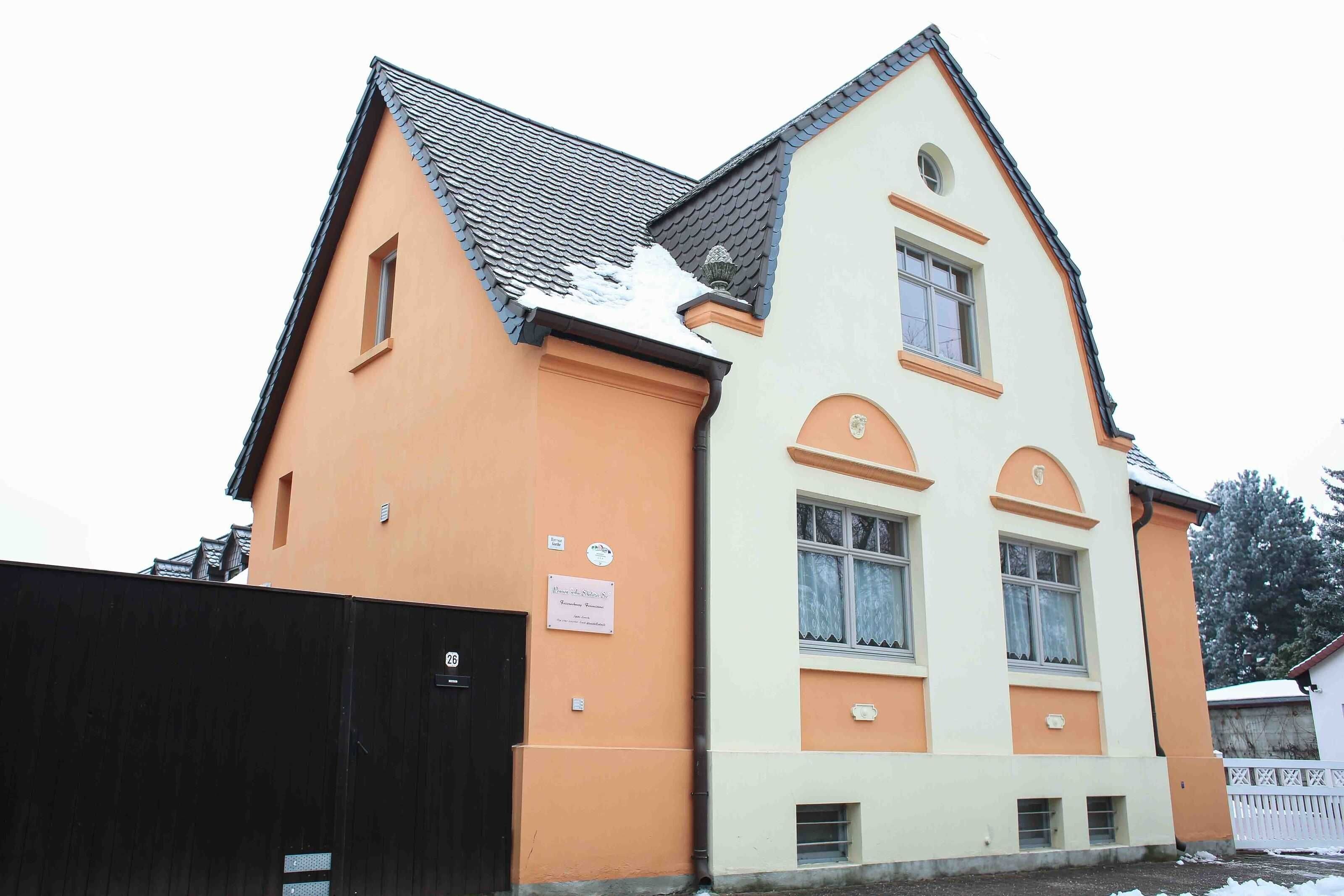 Ein zweistöckiges Gebäude mit einem geneigten Dach, einem schwarzen Tor und einem Schild an der Wand.