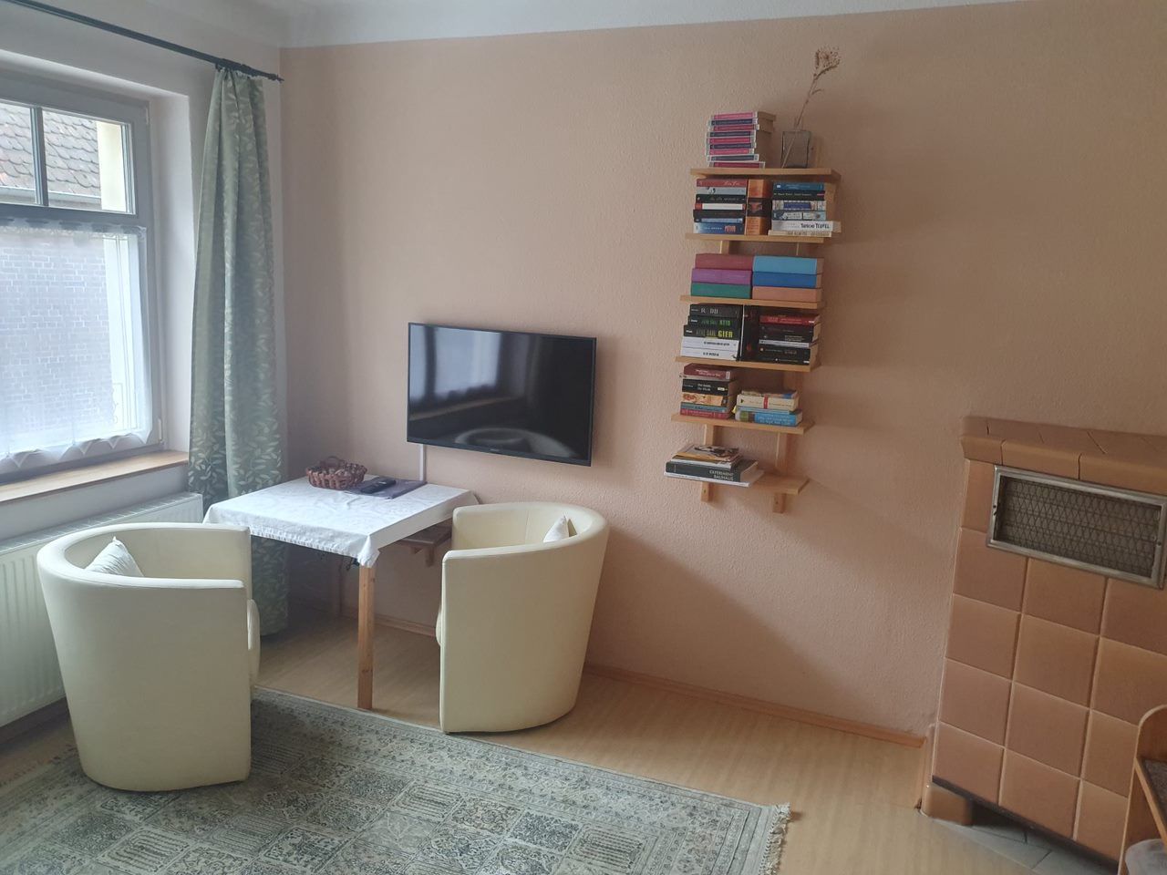 Une pièce avec un téléviseur, une petite table, deux chaises, une bibliothèque et un radiateur.