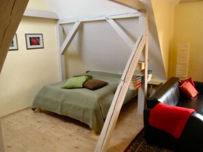 Een knus kamertje met een bed, een bank en een boekenplank.