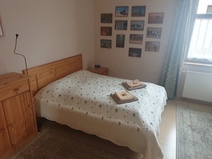 A bedroom with a wooden headboard, a bed with a floral bedspread, and a wall with framed pictures.