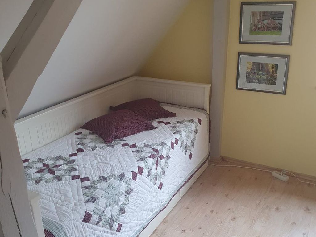 Ein Schlafzimmer mit einem Bett, einem weißen Kopfteil, einer gelben Wand und zwei gerahmten Bildern.