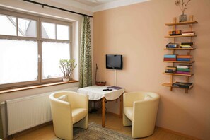 A room with a table, two chairs, a TV, a bookshelf, and a window with curtains.