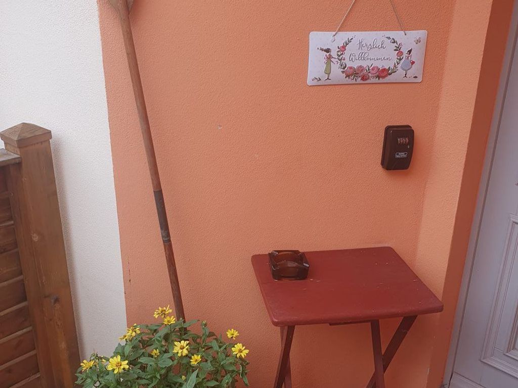 A small outdoor area with a wooden table, a hanging welcome sign, and a mailbox.