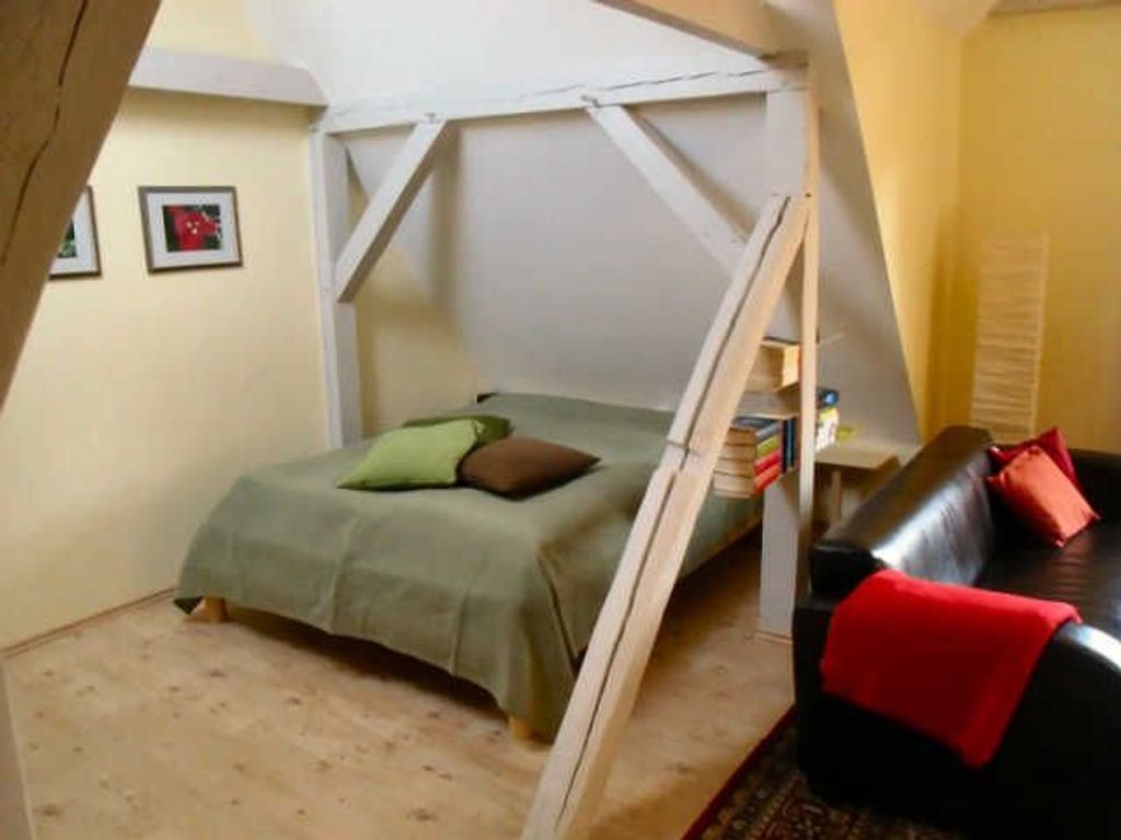A bedroom with a bed, a sofa, a small table, and a window.