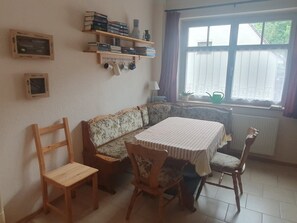 Un espace repas comprenant une table, des chaises, un canapé et des étagères où sont disposés des livres et des objets décoratifs.