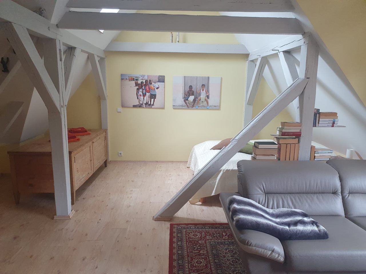 A loft bedroom with a sloped ceiling, a sofa, a bed, a wooden desk, and two framed photos on the wall.