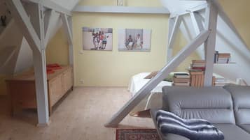 A loft bedroom with a sloped ceiling, a sofa, a bed, a wooden desk, and two framed photos on the wall.