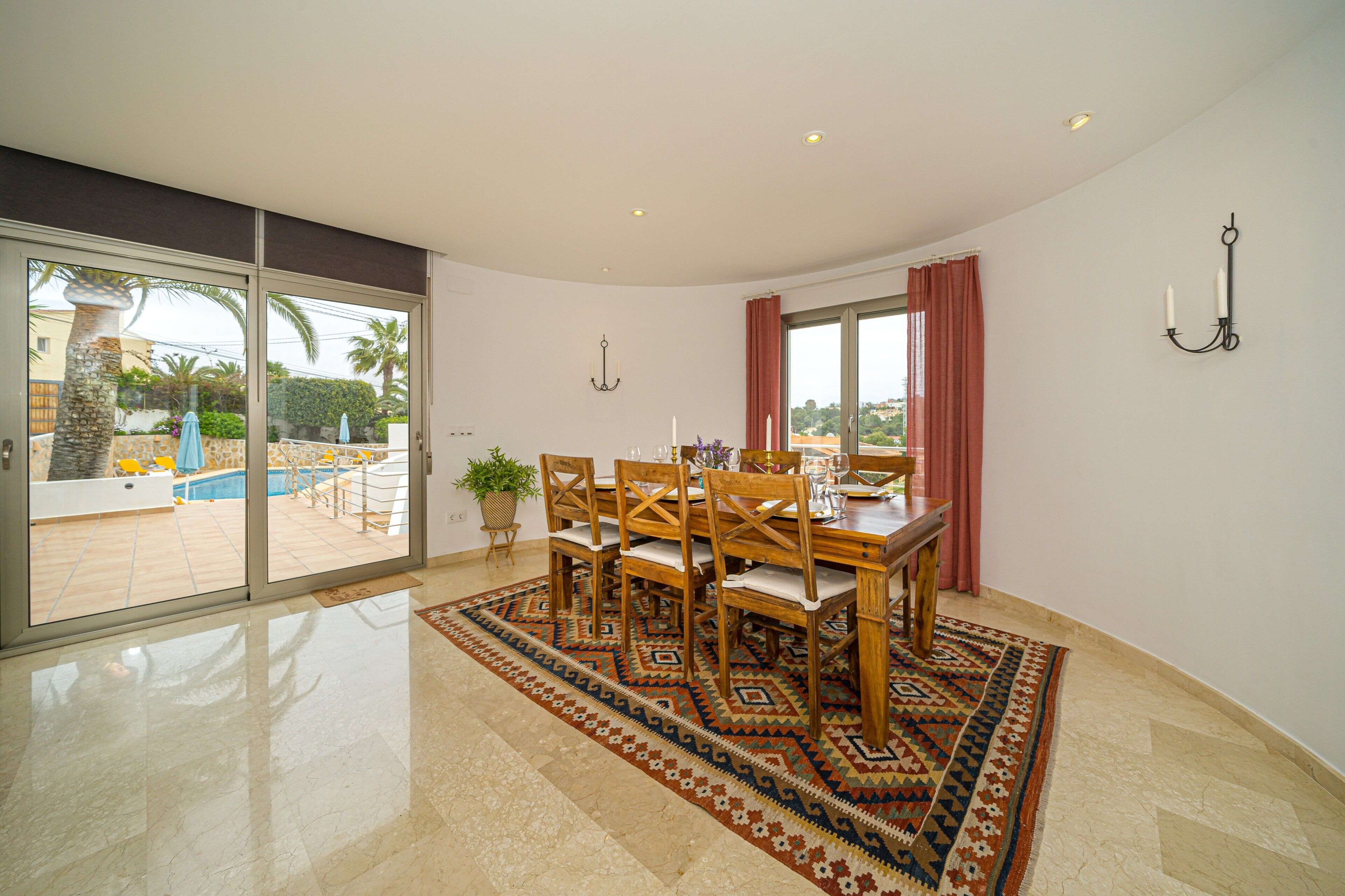 Un espace repas comprenant une table et des chaises, un tapis à motifs et une vue sur une piscine, visible à travers des portes vitrées.