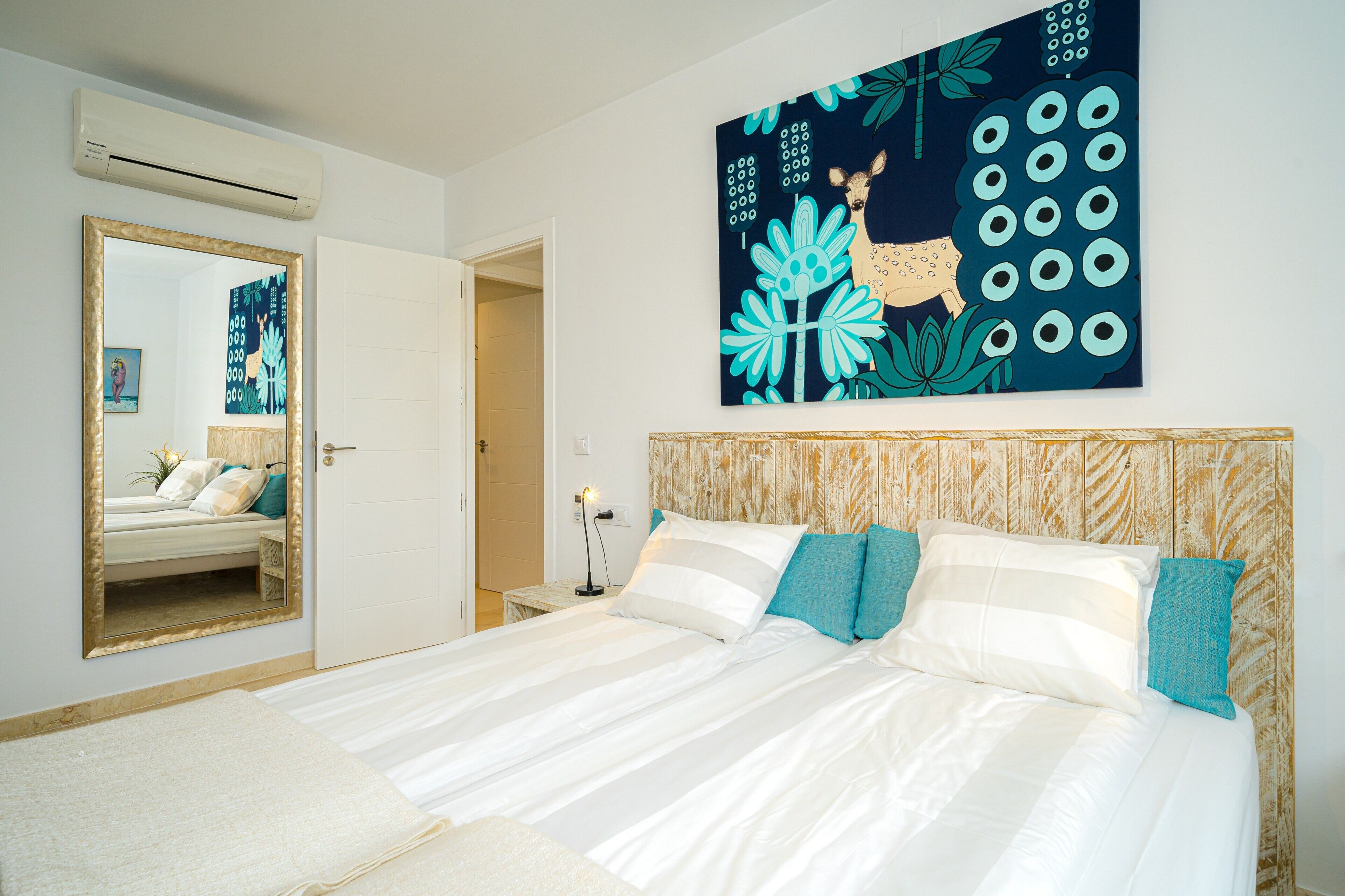 Une chambre à coucher avec un grand lit, un miroir, une œuvre d’art murale et une porte donnant sur une autre pièce.
