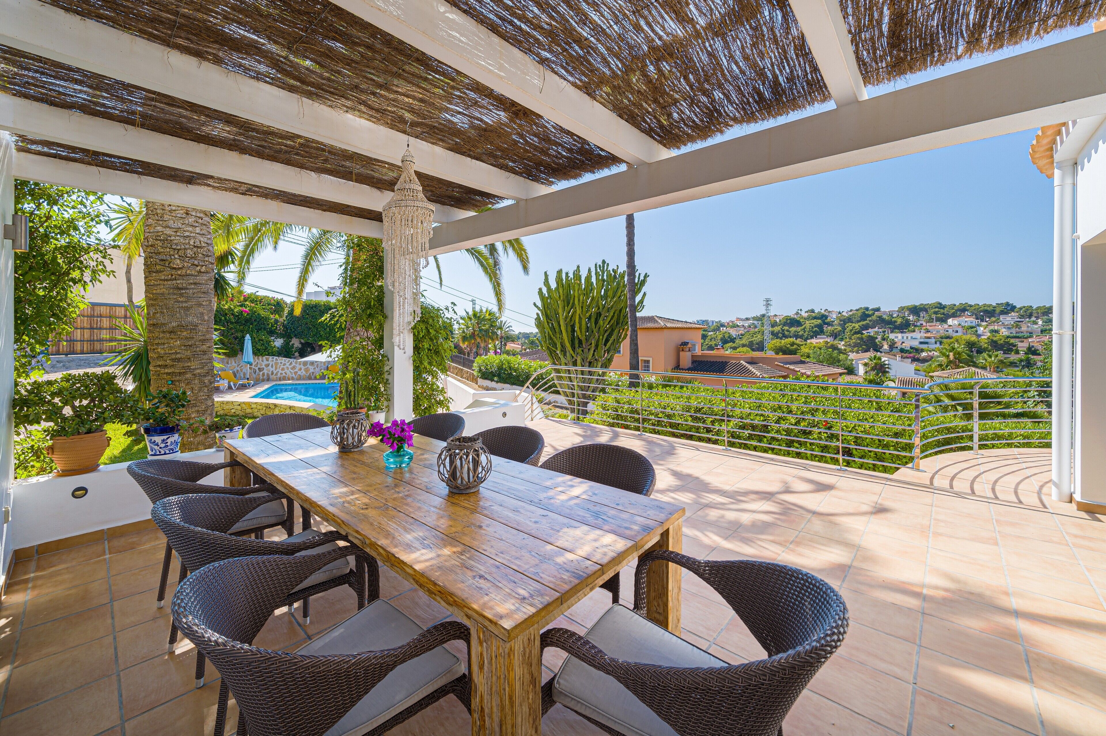 Une terrasse couverte, avec une table en bois et des chaises en osier, donnant sur une piscine et offrant une vue panoramique sur la ville.
