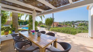 Une terrasse couverte, avec une table en bois et des chaises en osier, donnant sur une piscine et offrant une vue panoramique sur la ville.