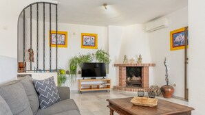 Ein Wohnzimmer mit einer Couch, einem Fernseher auf einem Schrank, einem Kamin und einer Treppe.