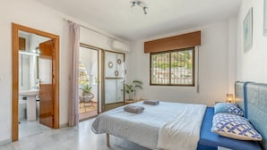 Ein Schlafzimmer mit einem Bett, einem Nachttisch, einem Fenster und einem durch eine offene Tür einsehbaren Badezimmer.