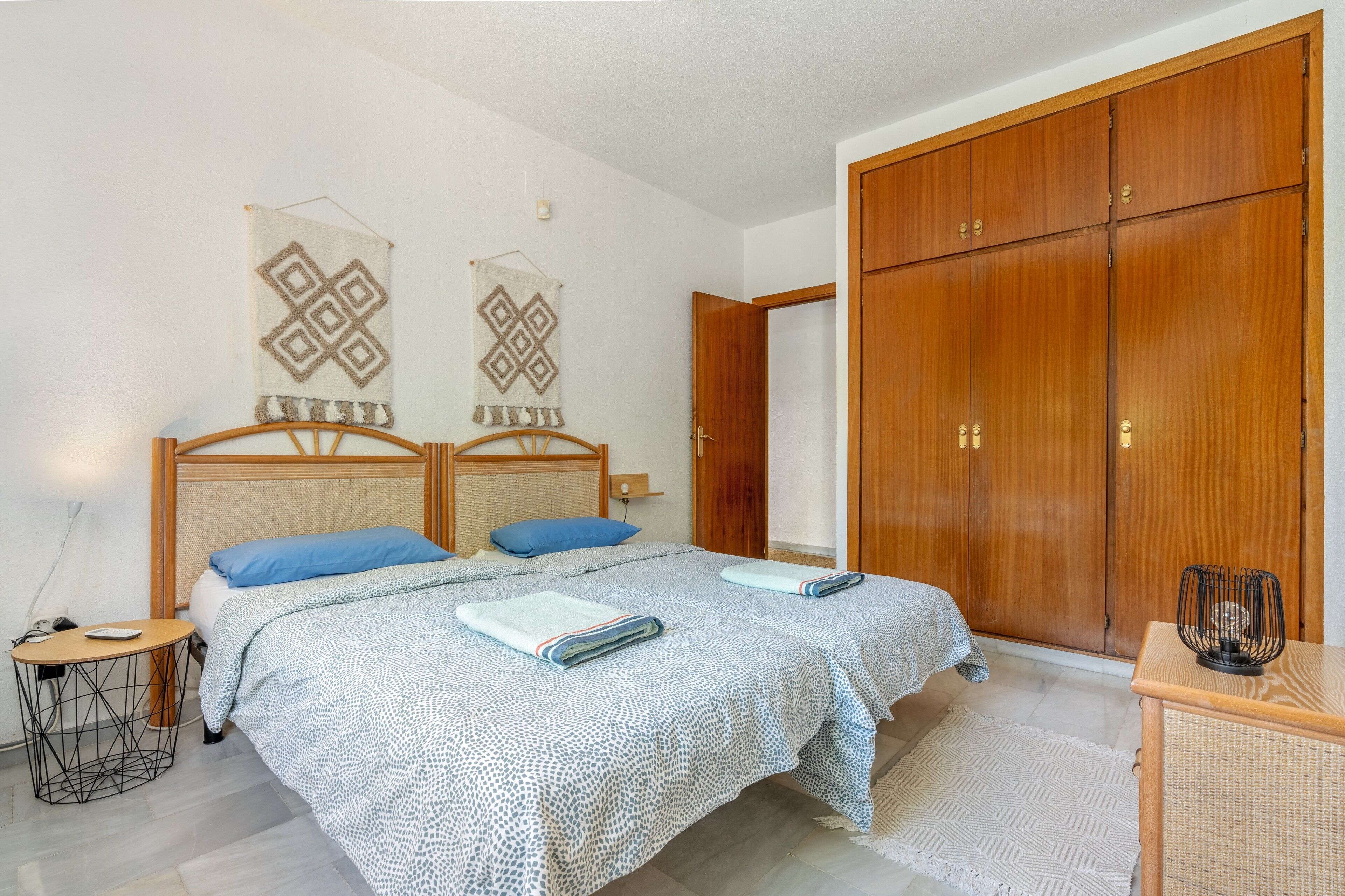 Un dormitorio con dos camas, un armario de madera, una mesita y un cuadro colgado en la pared.