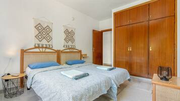 Un dormitorio con dos camas, un armario de madera, una mesita y un cuadro colgado en la pared.