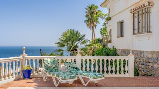 Ein Poolbereich mit Liegestühlen, einer Pflanze im Topf und Blick auf das Meer.